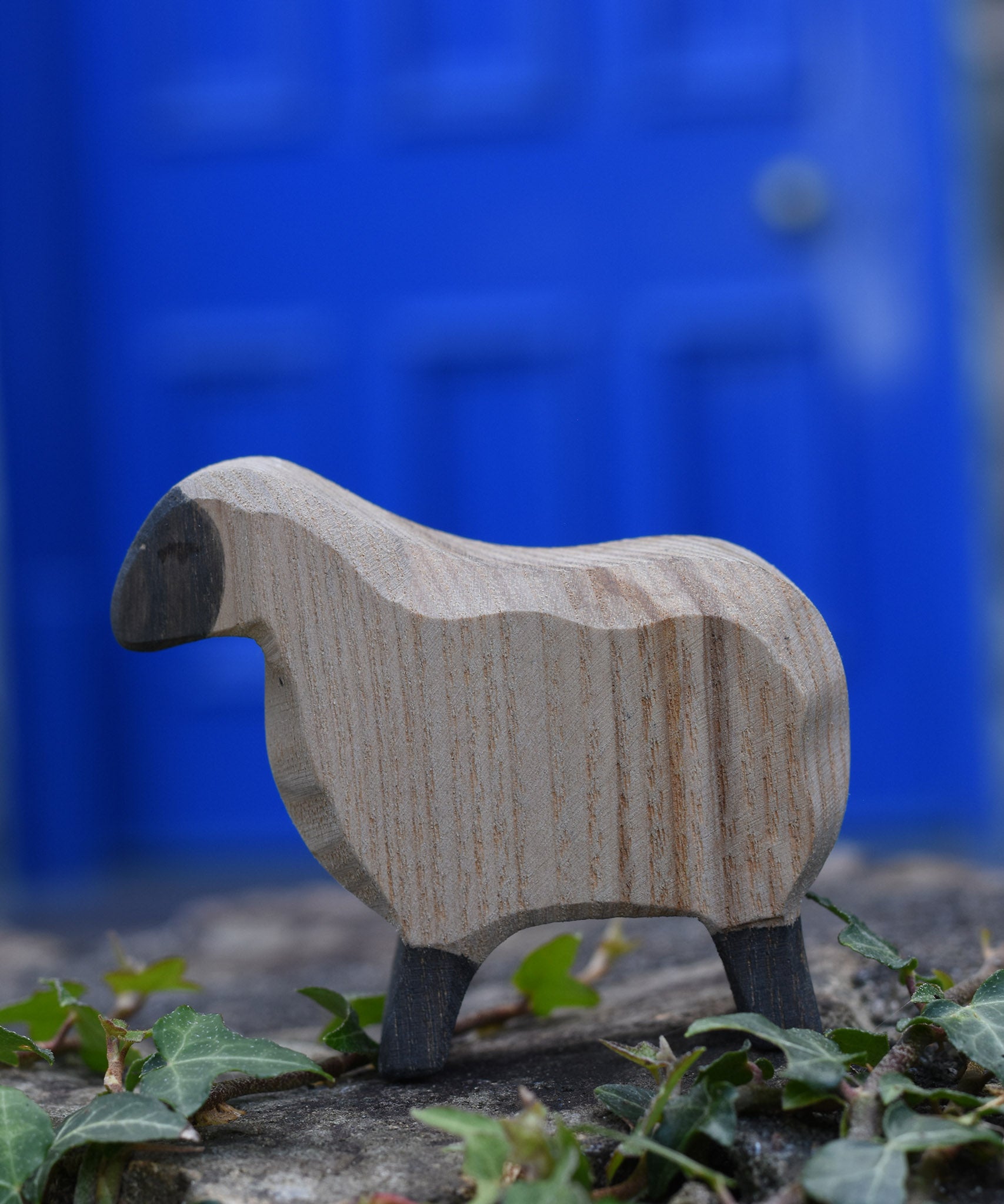 An Ostheimer moorland sheep placed on a stone wall outdoors. These wooden figures are part of a large range of expertly hand crafted, Waldorf inspired, wooden toys here at Babipur.