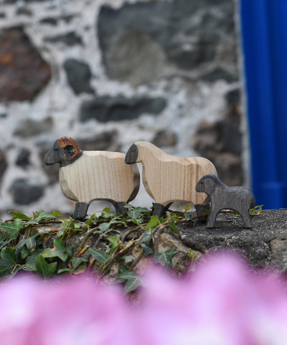 An Ostheimer wooden ram, sheep and lamb all placed on a wooden wall outdoors. These wooden figures are part of a large range of expertly hand crafted, Waldorf inspired, wooden toys here at Babipur. 