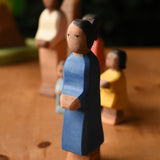 An Ostheimer mother wooden toy figure with brown skin placed at the front of a small world play scene. These wooden figures are part of a wide range of expertly hand crafted wooden toys here at Babipur.