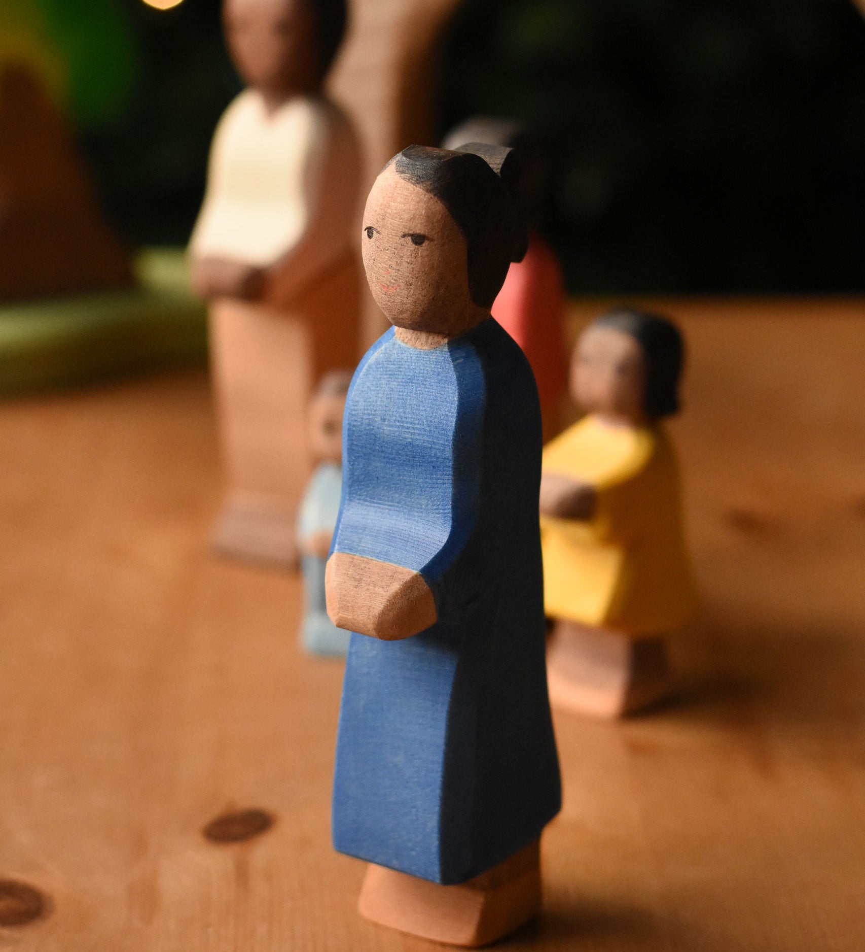 An Ostheimer mother wooden toy figure with brown skin placed at the front of a small world play scene. These wooden figures are part of a wide range of expertly hand crafted wooden toys here at Babipur.