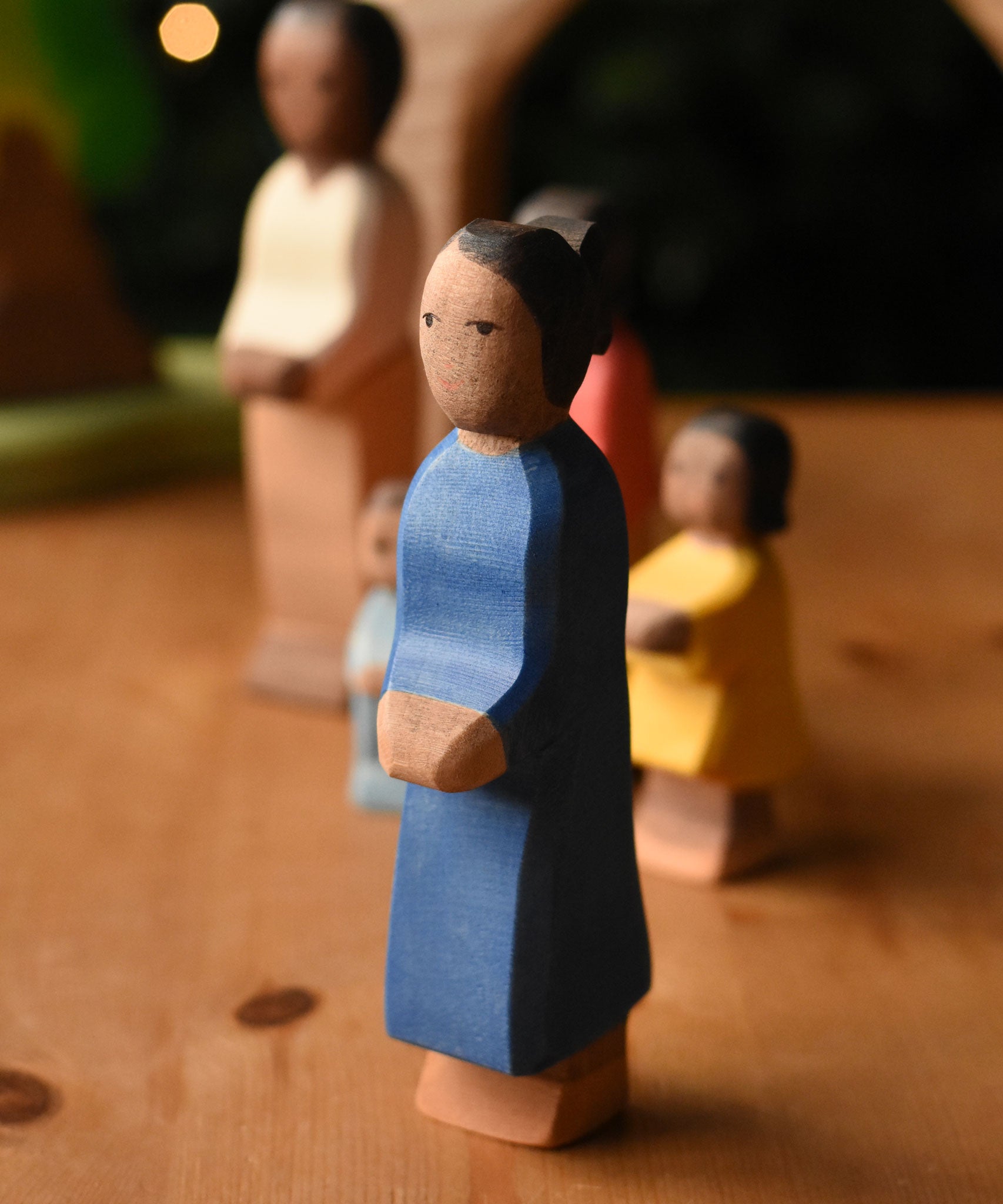 An Ostheimer mother wooden toy figure with brown skin placed at the front of a small world play scene. These wooden figures are part of a wide range of expertly hand crafted wooden toys here at Babipur.