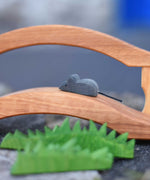 An Ostheimer mouse figure placed on a wooden toy bridge, Ostheimer wooden toy grass can be seen in the foreground of the photo. 