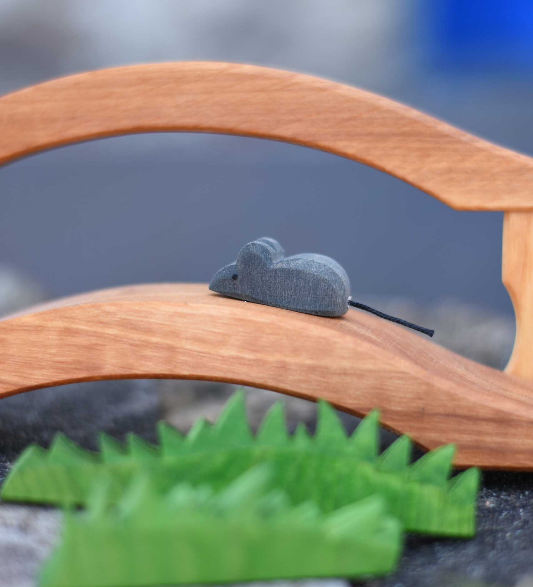 An Ostheimer mouse figure placed on a wooden toy bridge, Ostheimer wooden toy grass can be seen in the foreground of the photo. 