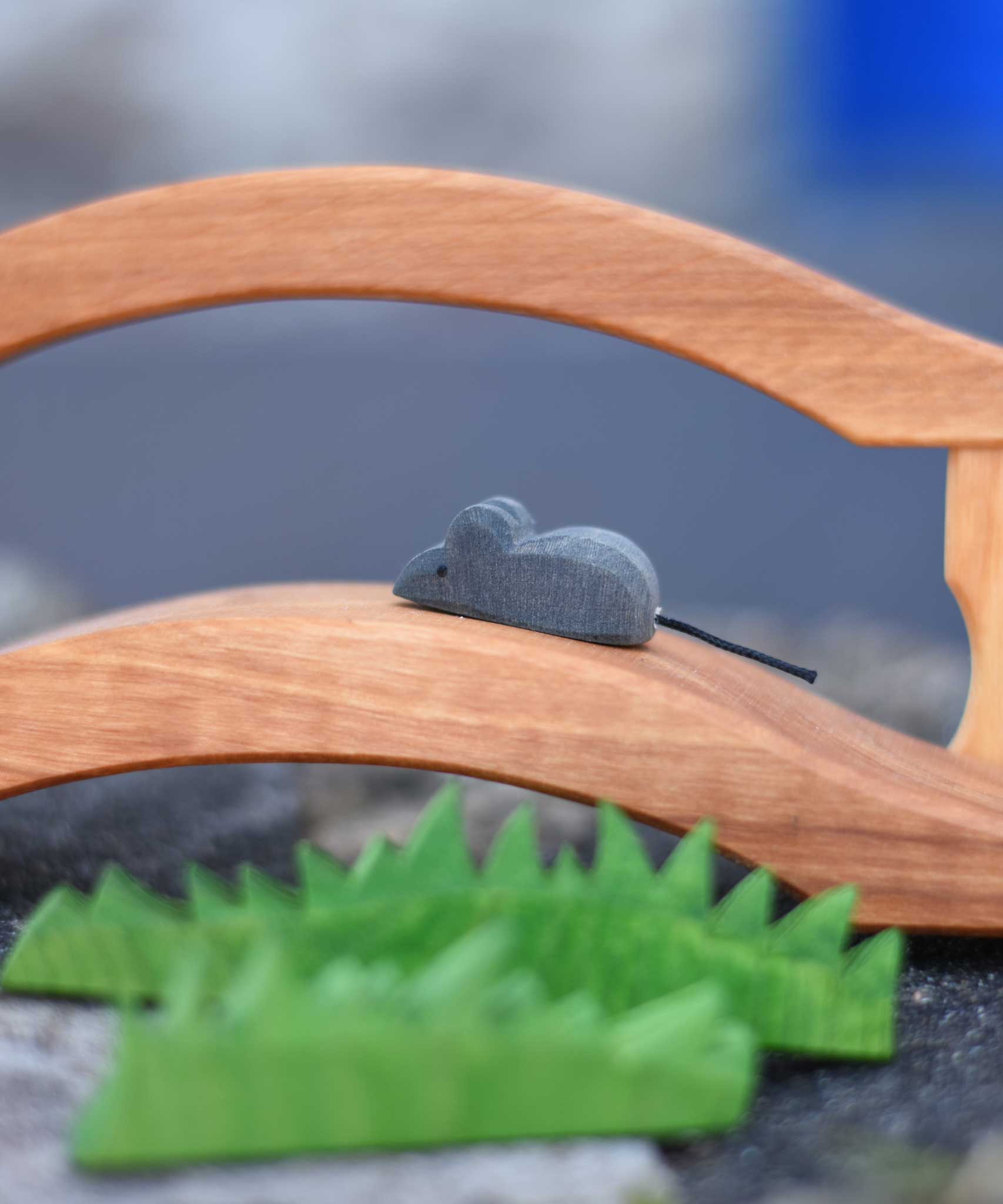 An Ostheimer mouse figure placed on a wooden toy bridge, Ostheimer wooden toy grass can be seen in the foreground of the photo. 