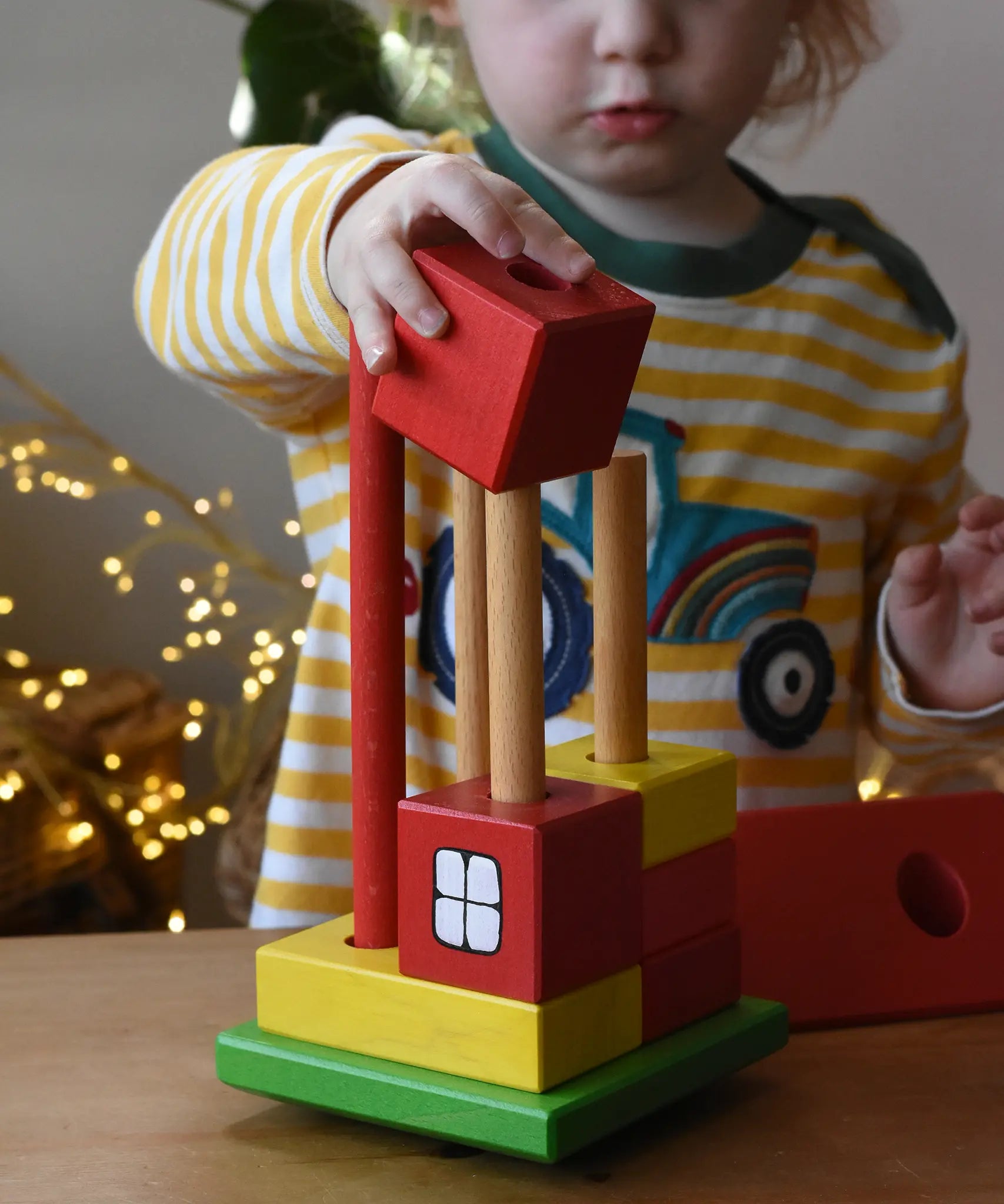 Ostheimer multi coloured block house wooden toy, child placing he blocks onto the poles.