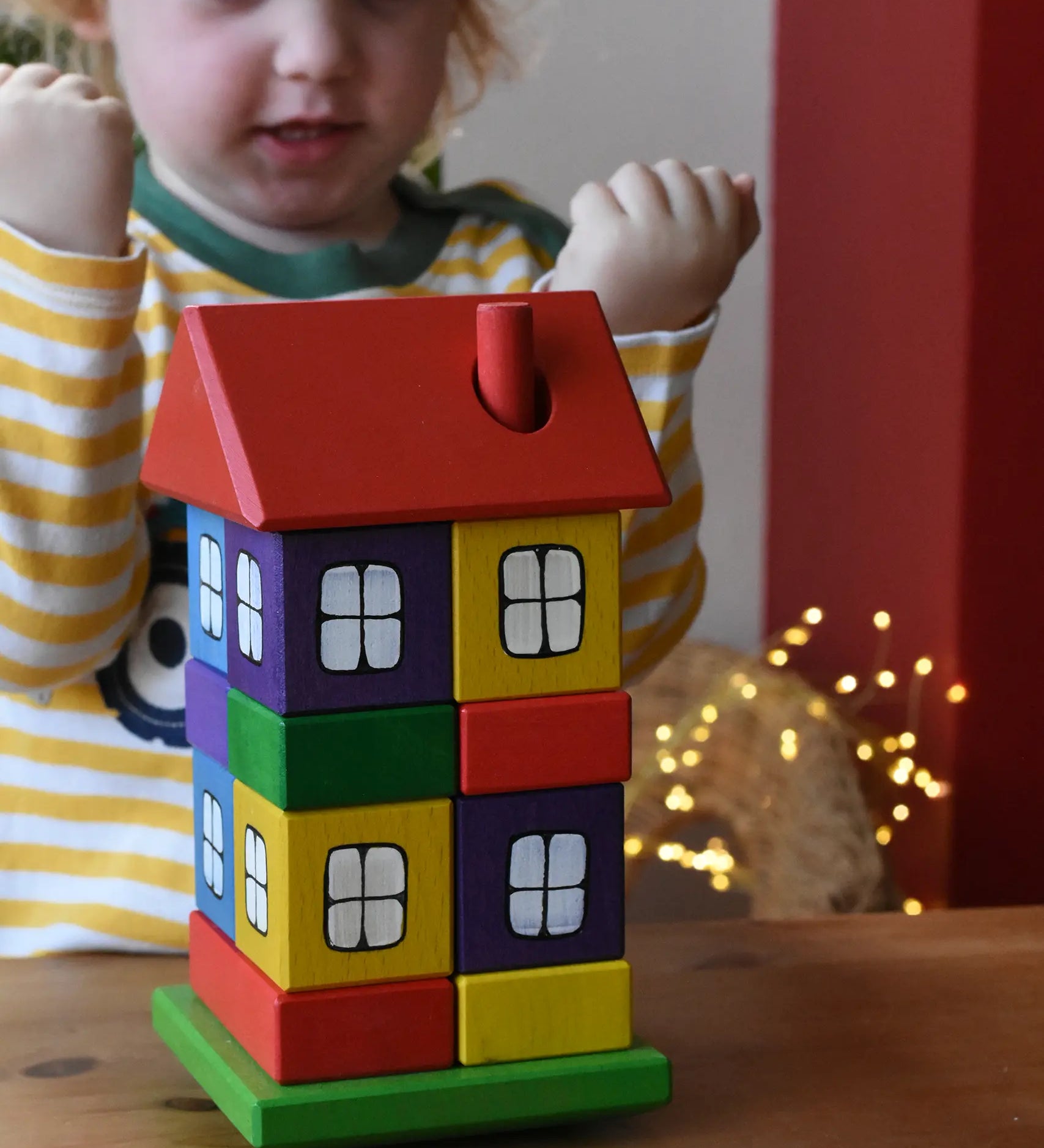 Ostheimer multi coloured block house stacker toy. Child cheering in the background.