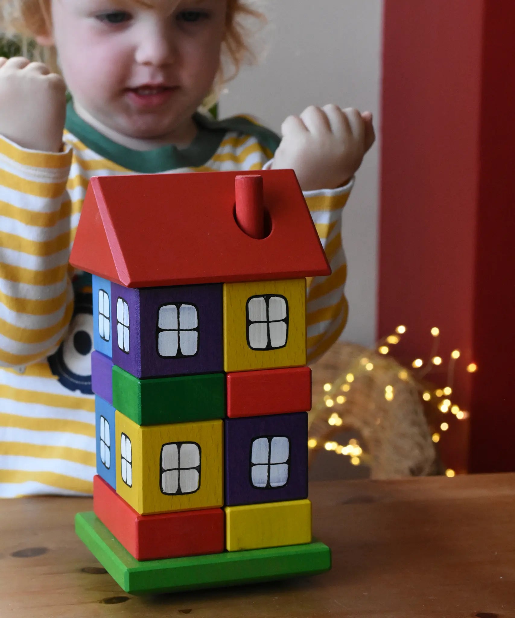 Ostheimer multi coloured block house stacker toy. Child cheering in the background.