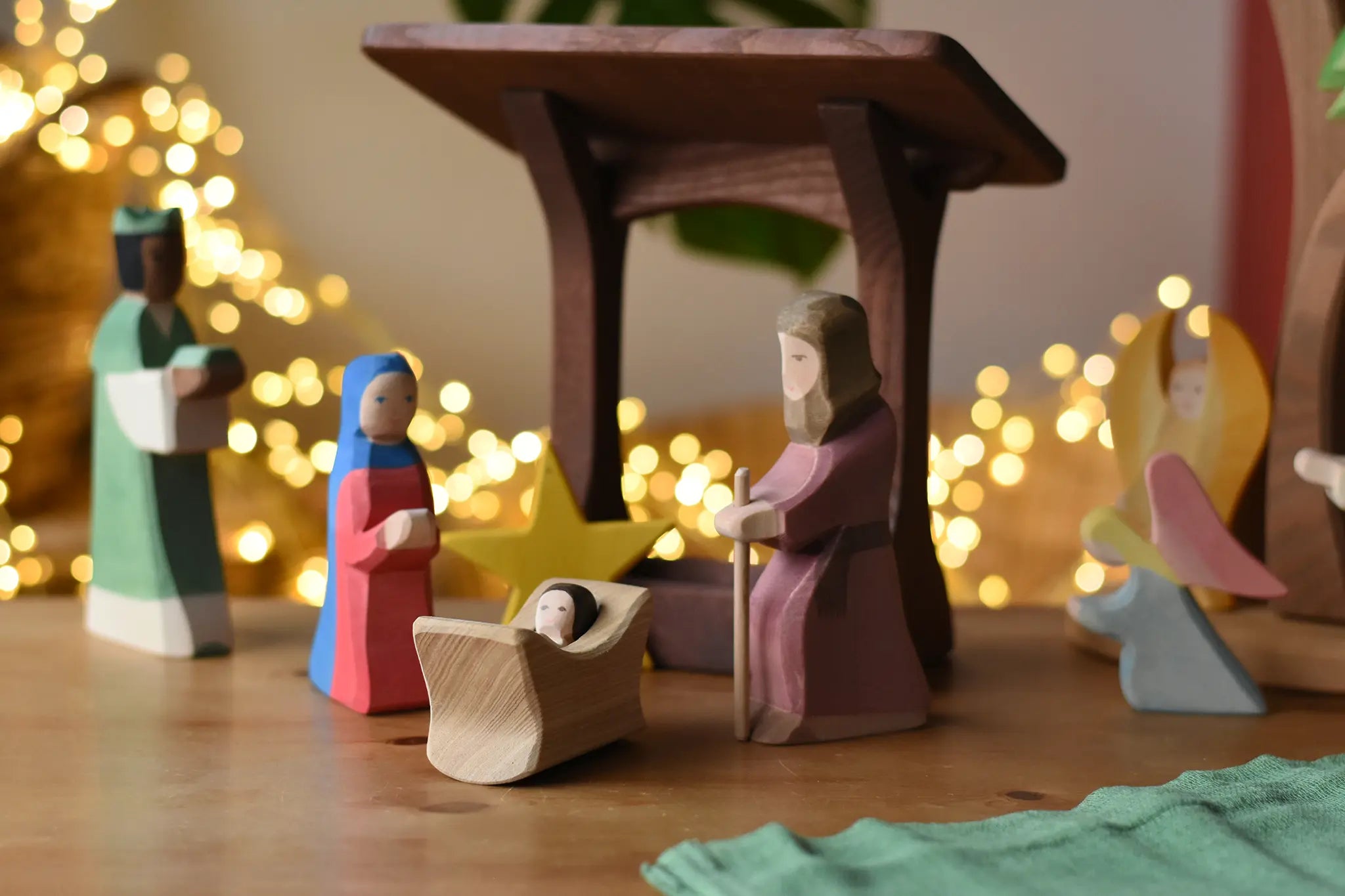 Ostheimer Mary and Joseph wooden toy figures in a festive nativity small world play scene with fairy lights in the background.