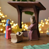 Ostheimer Mary and Joseph wooden toy figures in a festive nativity small world play scene with fairy lights in the background.