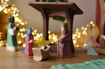 Ostheimer Mary and Joseph wooden toy figures in a festive nativity small world play scene with fairy lights in the background.
