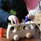 Close up of a child playing with the Ostheimer Natural Bus With 4 People. The child is placing the colourful wooden figures into the slots on the bus. 