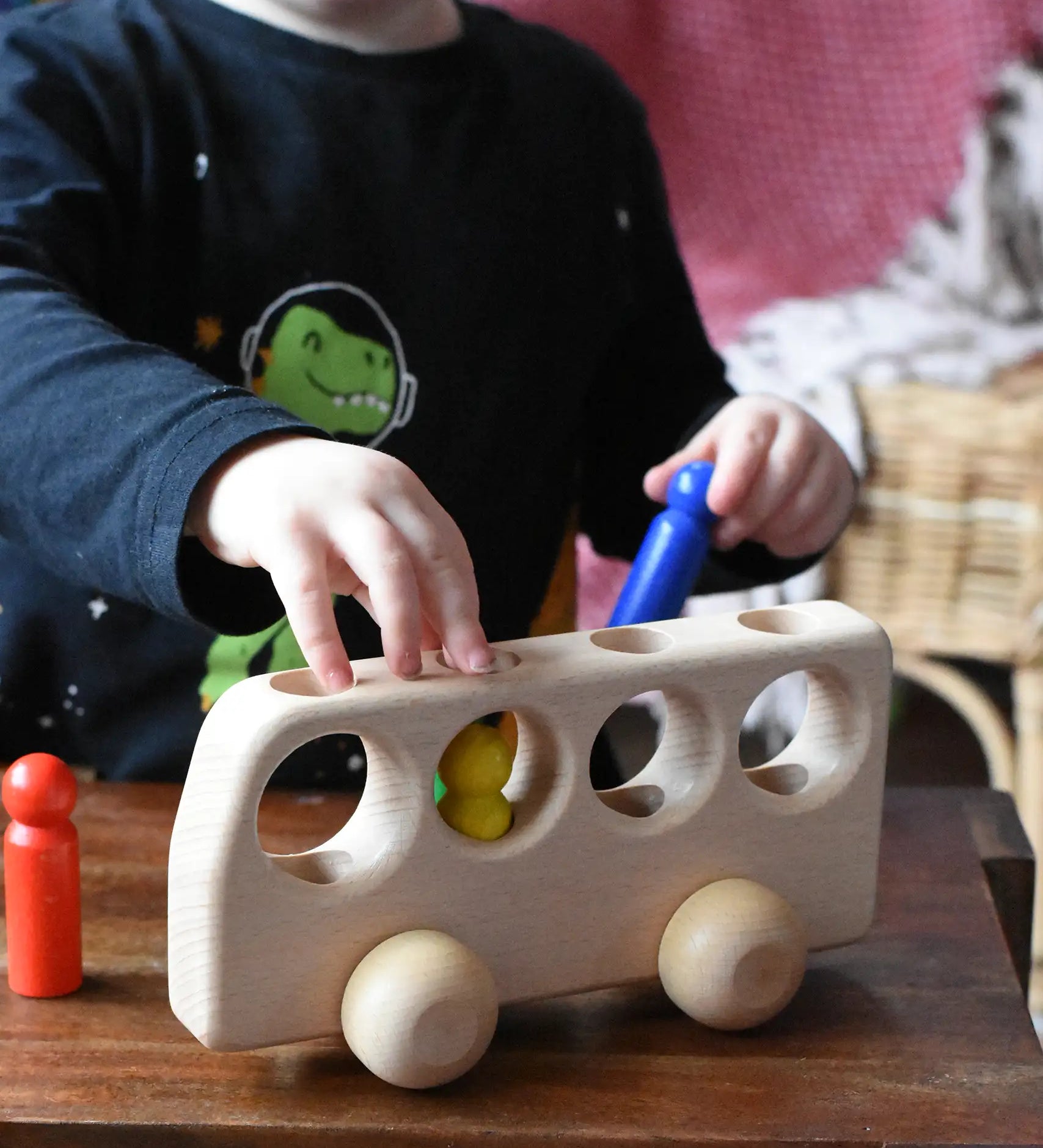 Close up of a child playing with the Ostheimer Natural Bus With 4 People. The child is placing the colourful wooden figures into the slots on the bus. 