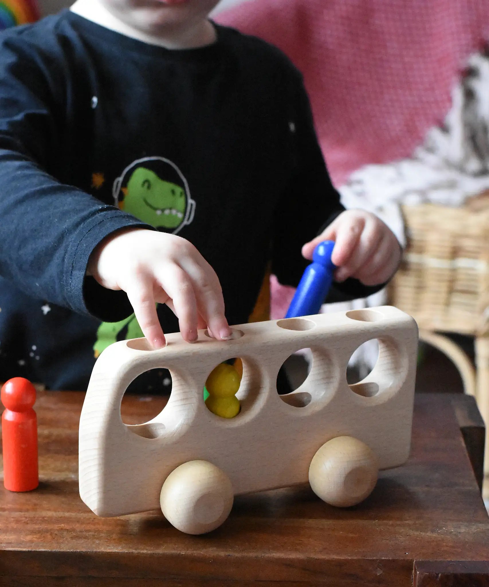 Close up of a child playing with the Ostheimer Natural Bus With 4 People. The child is placing the colourful wooden figures into the slots on the bus. 
