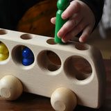 Close up of a child playing with the Ostheimer Natural Bus With 4 People. The child is placing the green coloured wooden figures into one of the circular shaped slots on the top of the bus. 