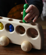 Close up of a child playing with the Ostheimer Natural Bus With 4 People. The child is placing the green coloured wooden figures into one of the circular shaped slots on the top of the bus. 