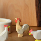 Ostheimer ochre rooster wooden toy figure placed besides a white village well.