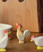 Ostheimer ochre rooster wooden toy figure placed besides a white village well.
