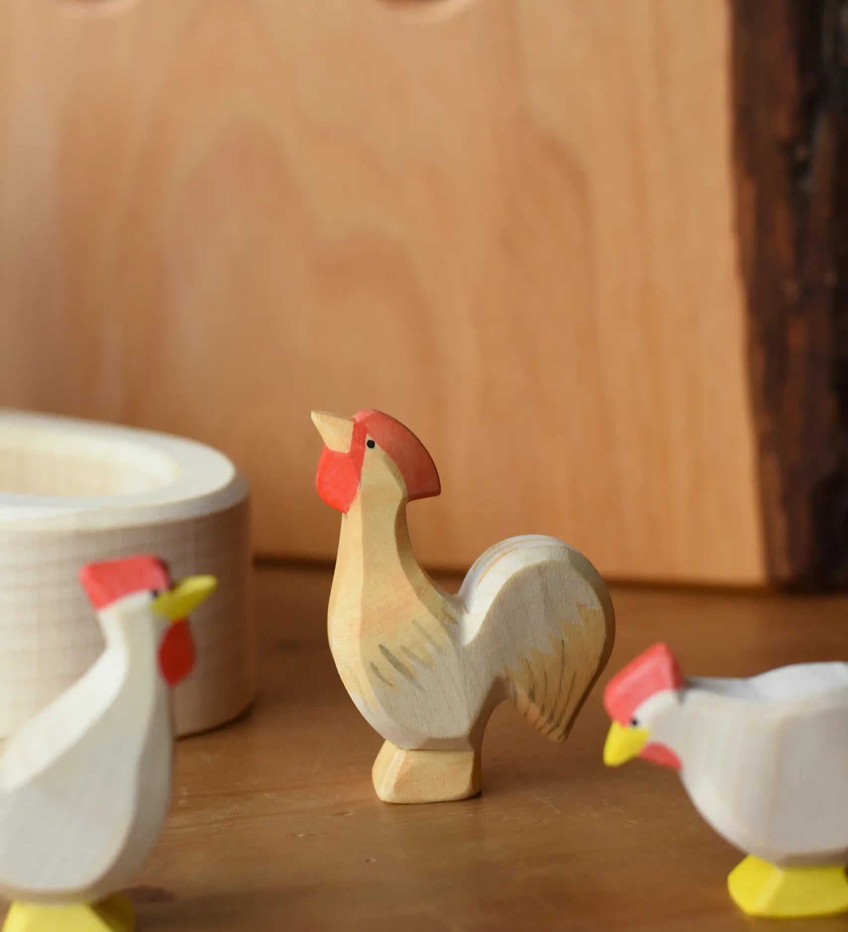 Ostheimer ochre rooster wooden toy figure placed besides a white village well.