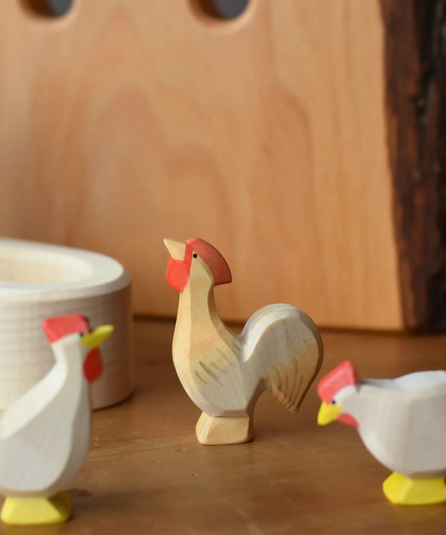Ostheimer ochre rooster wooden toy figure placed besides a white village well.
