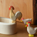 Ostheimer ochre rooster wooden toy figure standing on the side of a white village well.