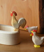 Ostheimer ochre rooster wooden toy figure standing on the side of a white village well.