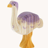 Ostheimer Ostrich wooden toy figure pictured at a slight angle. The photo shows the natural wood grain detail on the handcarfted figure. The ostrich has a white base, light yellow orange legs and beak and purple coloured details.