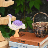 An Ostheimer wooden ostrich toy figure placed on a pile of books, the bird tree can be seen in the background. 