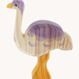 A side view of Ostheimer Ostrich wooden toy figure. The photo shows the natural wood grain detail on the handcrafted figure. The ostrich has a white base, light yellow orange legs and beak and purple coloured details.