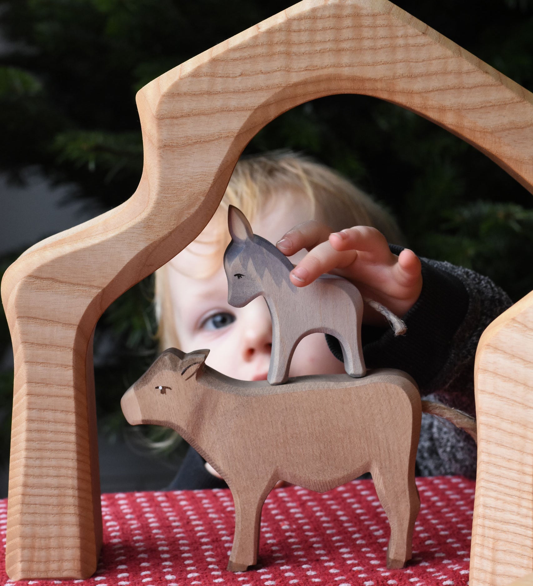 A child placing an Ostheimer small donkey figure on top of an Ostheimer ox figure. These wooden figures are part of a wide range of expertly hand crafted wooden toys here at Babipur. 
