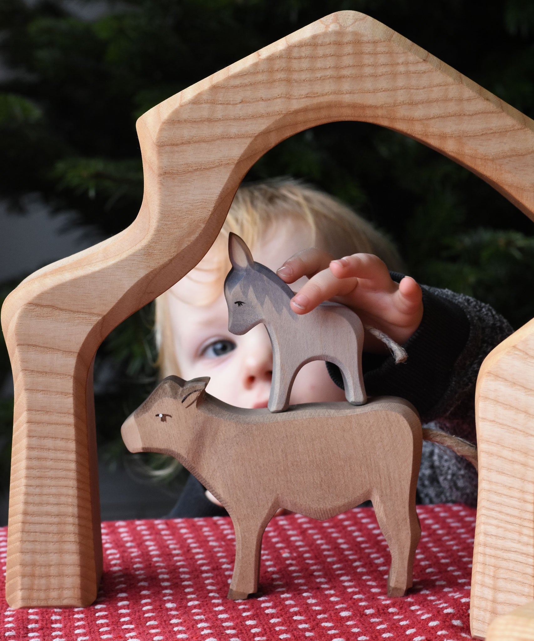 A child placing an Ostheimer small donkey figure on top of an Ostheimer ox figure. These wooden figures are part of a wide range of expertly hand crafted wooden toys here at Babipur. 