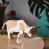 Ostheimer ox wooden toy figure placed on a wooden surface with a small spruce tree and standing ox in the background. 