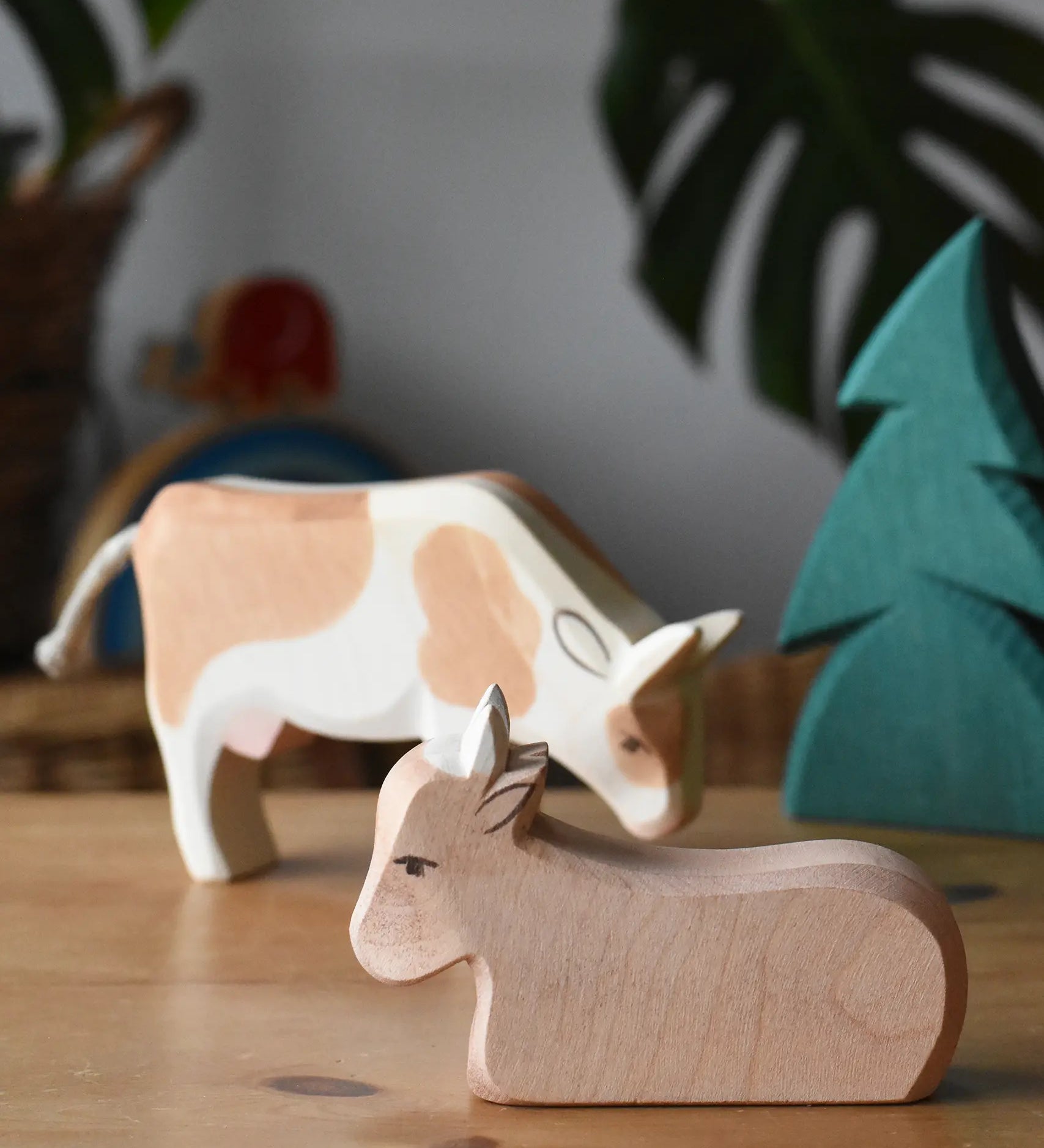 Ostheimer ox wooden toy figure placed on a wooden surface with a small spruce tree and standing ox in the background. 