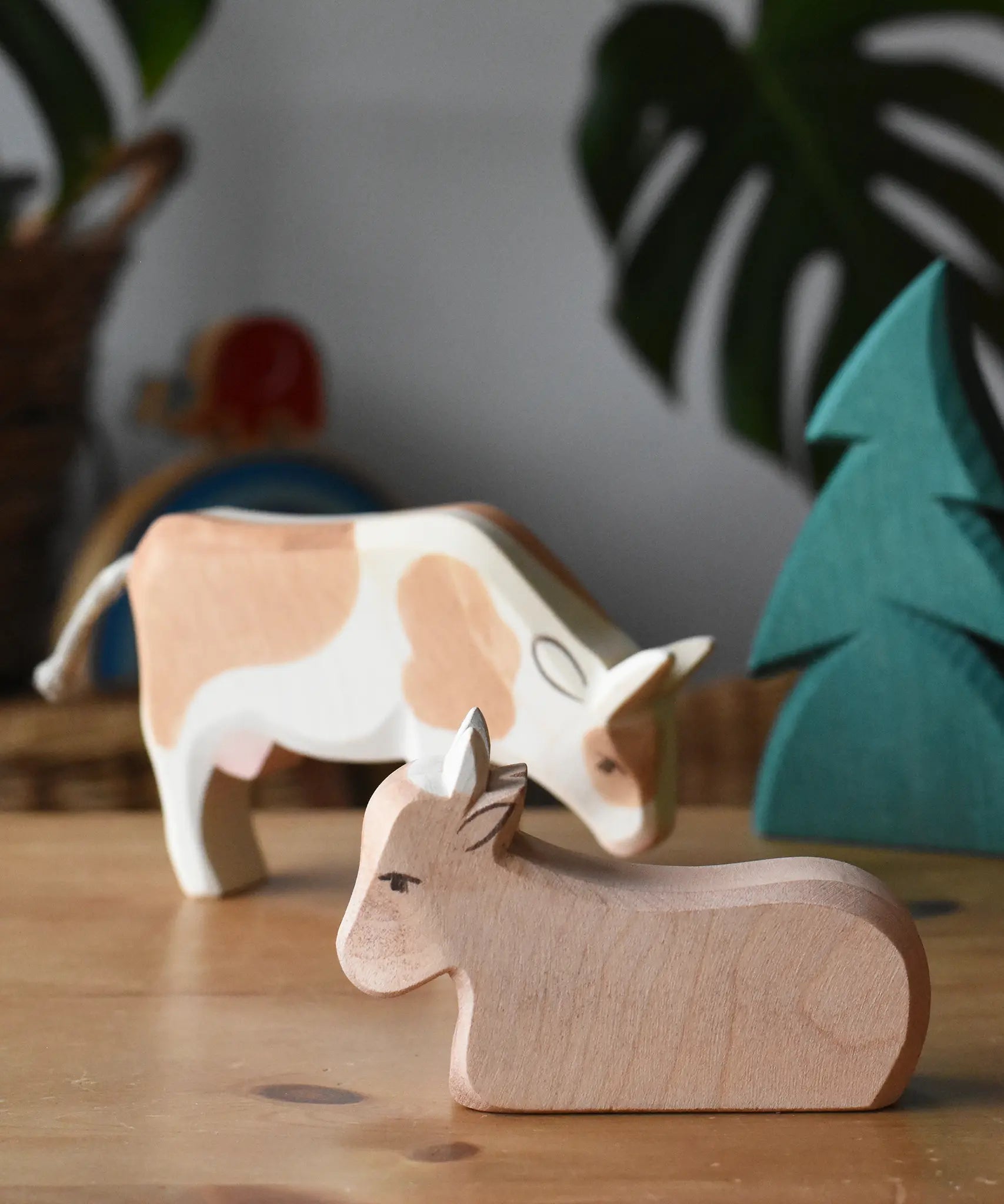 Ostheimer ox wooden toy figure placed on a wooden surface with a small spruce tree and standing ox in the background. 