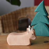 Ostheimer ox wooden toy figure placed on a wooden surface with a small spruce tree.