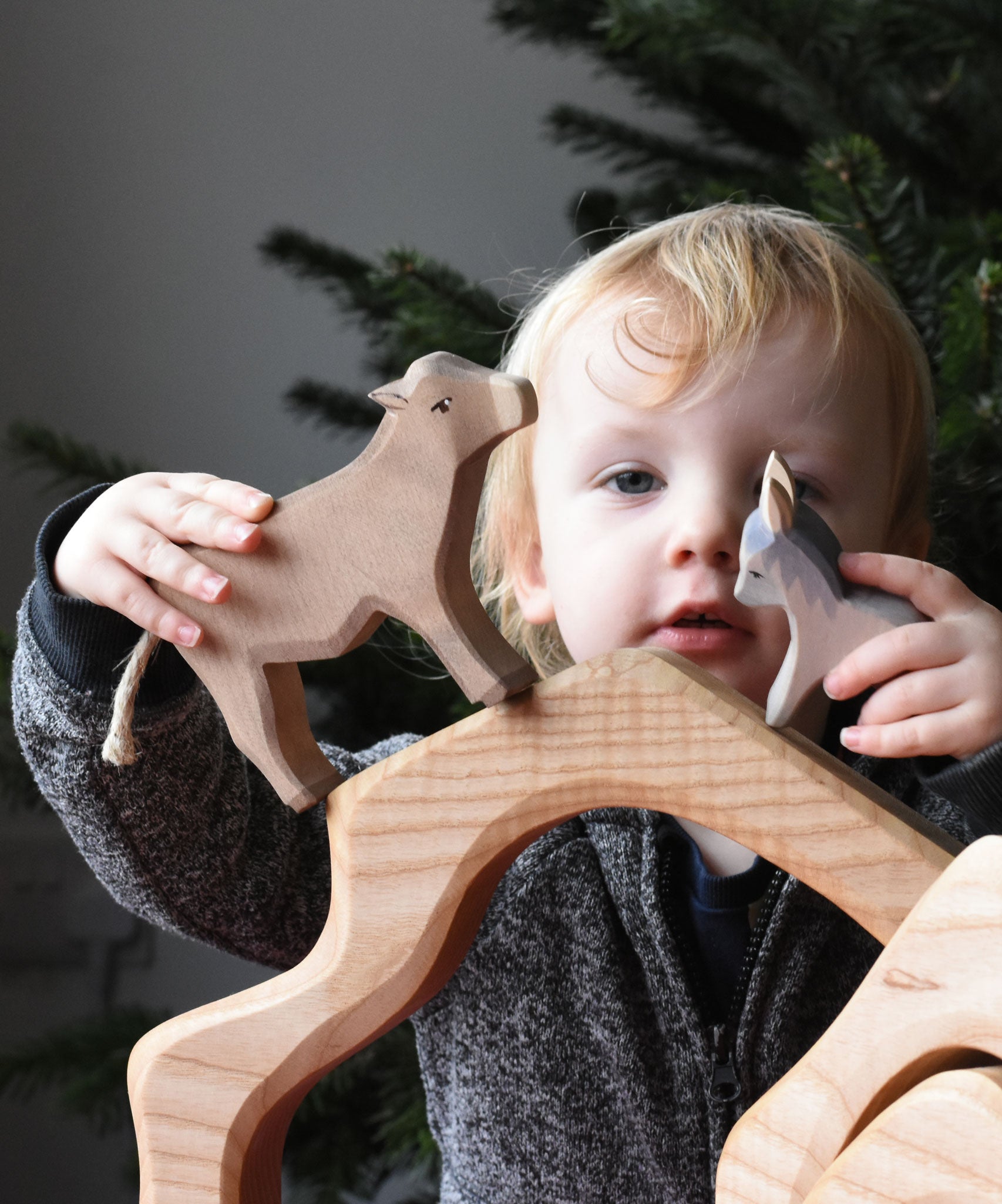 A child playing with an Ostheimer small donkey figure and an Ostheimer ox figure placing them on top of a wooden cave shaped piece. These wooden figures are part of a wide range of expertly hand crafted wooden toys here at Babipur.