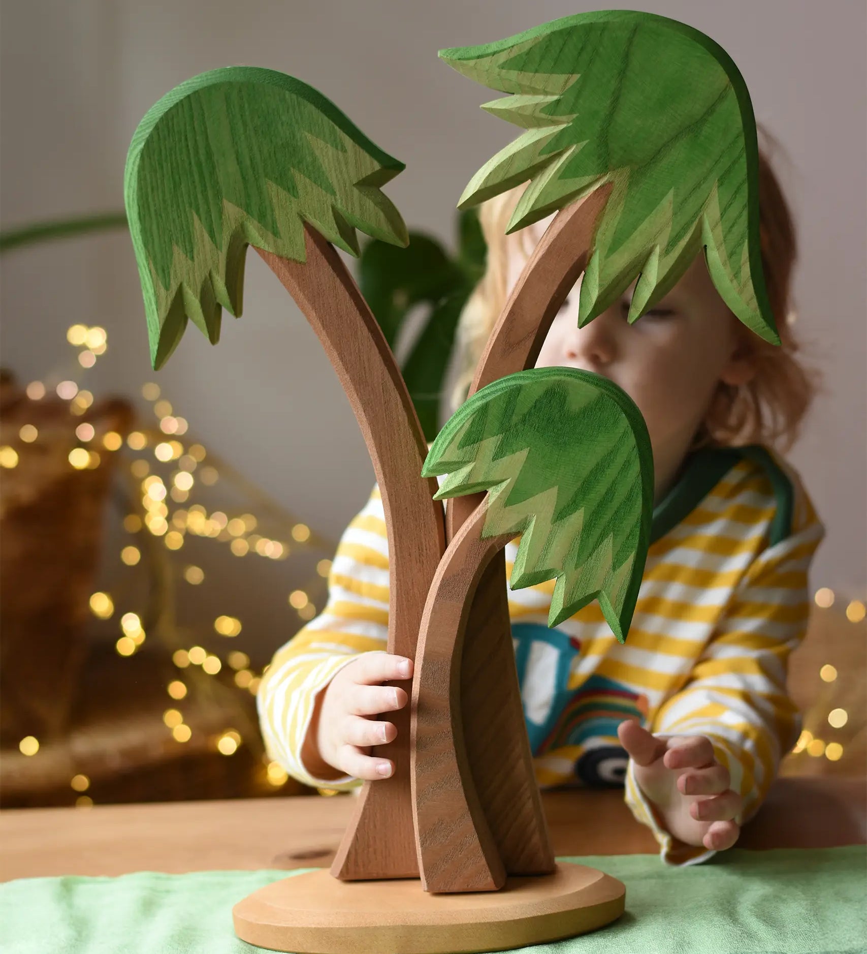 Ostheimer palm tree group with support base placed on a green cotton play cloth with a child standing behind it.