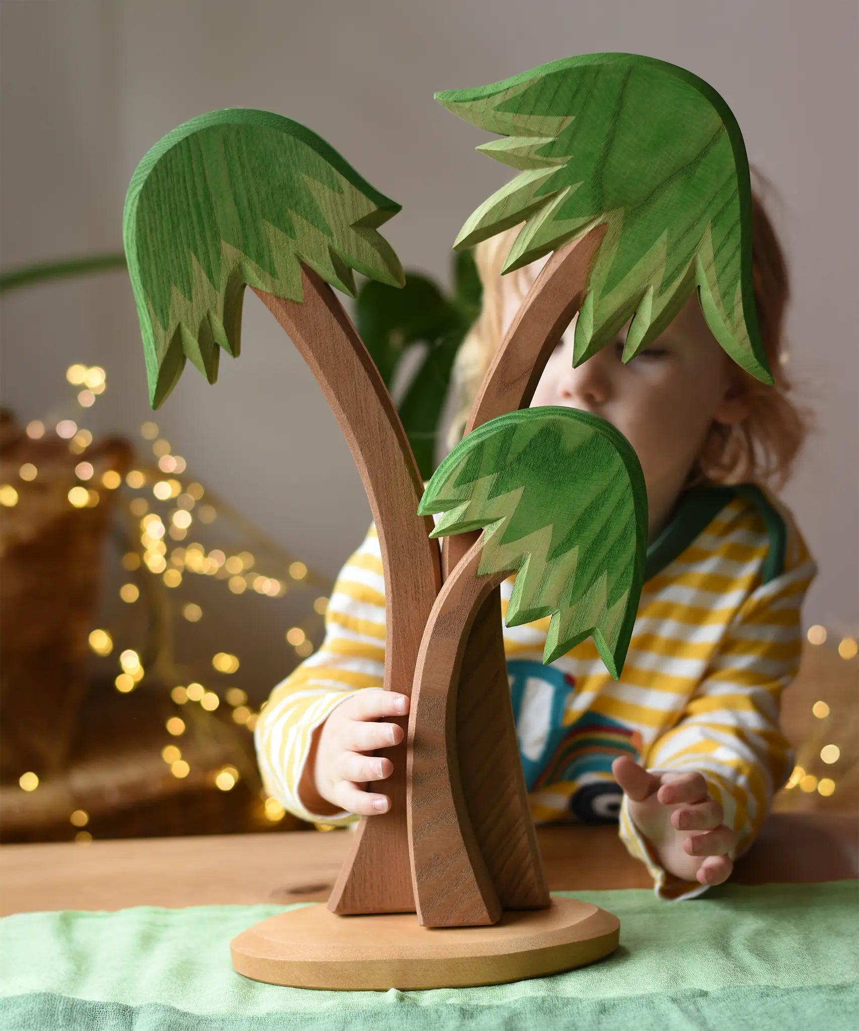 Ostheimer palm tree group with support base placed on a green cotton play cloth with a child standing behind it.