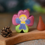 An Ostheimer hand made and hand painted wooden pansy Flower Child figure toy placed on a natural Grimm's celebration ring. These flower child wooden figures are part of a wide range of expertly hand crafted wooden toys here at Babipur.