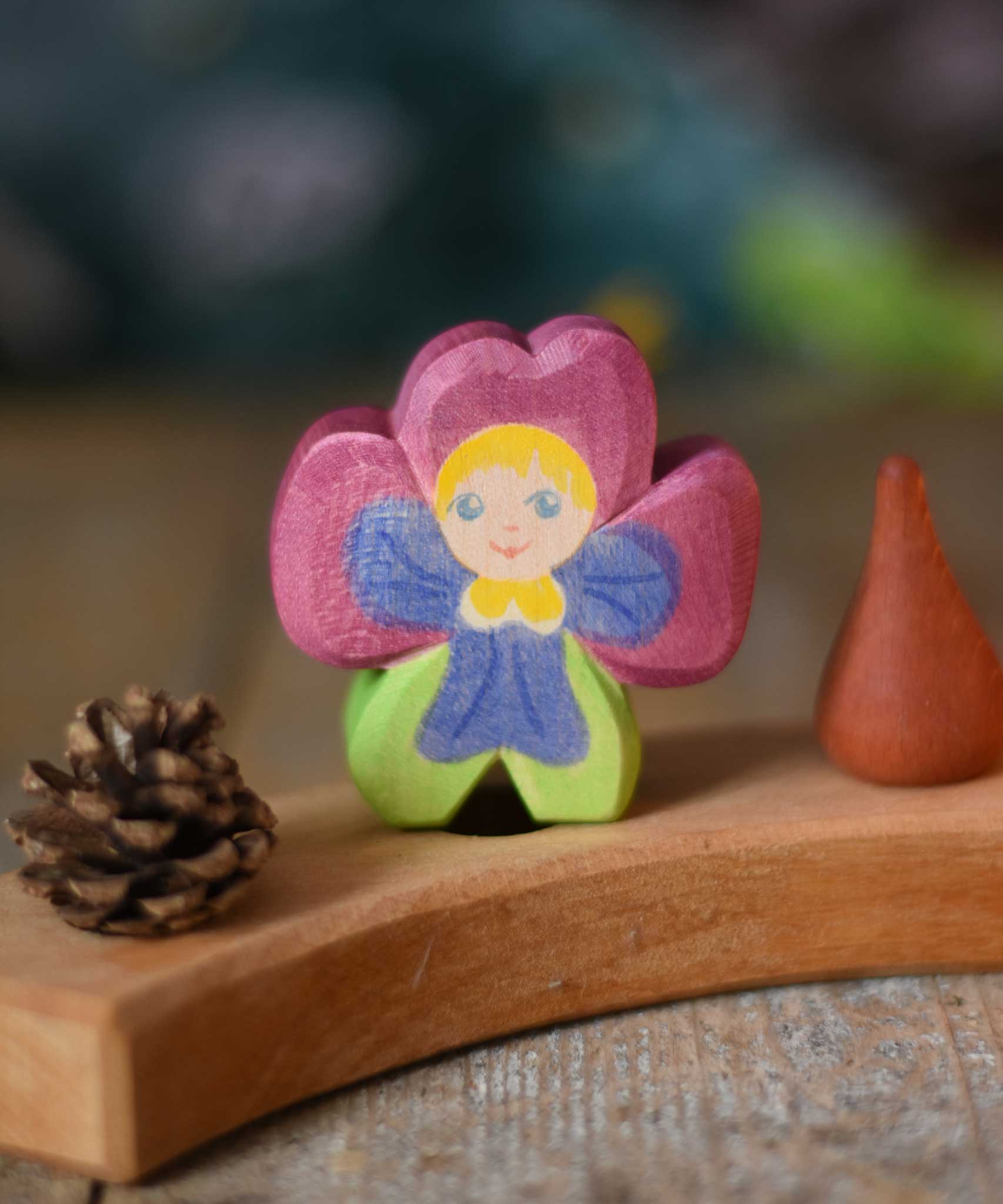 An Ostheimer hand made and hand painted wooden pansy Flower Child figure toy placed on a natural Grimm's celebration ring. These flower child wooden figures are part of a wide range of expertly hand crafted wooden toys here at Babipur.