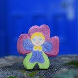 An Ostheimer hand made and hand painted wooden pansy Flower Child figure toy placed on a stone wall outdoors. These flower child wooden figures are part of a wide range of expertly hand crafted wooden toys here at Babipur. 