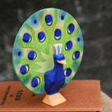 A Ostheimer peacock wooden toy figure with open feathers placed on a pile of books.