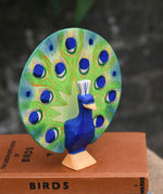 A Ostheimer peacock wooden toy figure with open feathers placed on a pile of books.