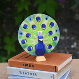 A Ostheimer peacock wooden toy figure with open feathers placed on a pile of books.