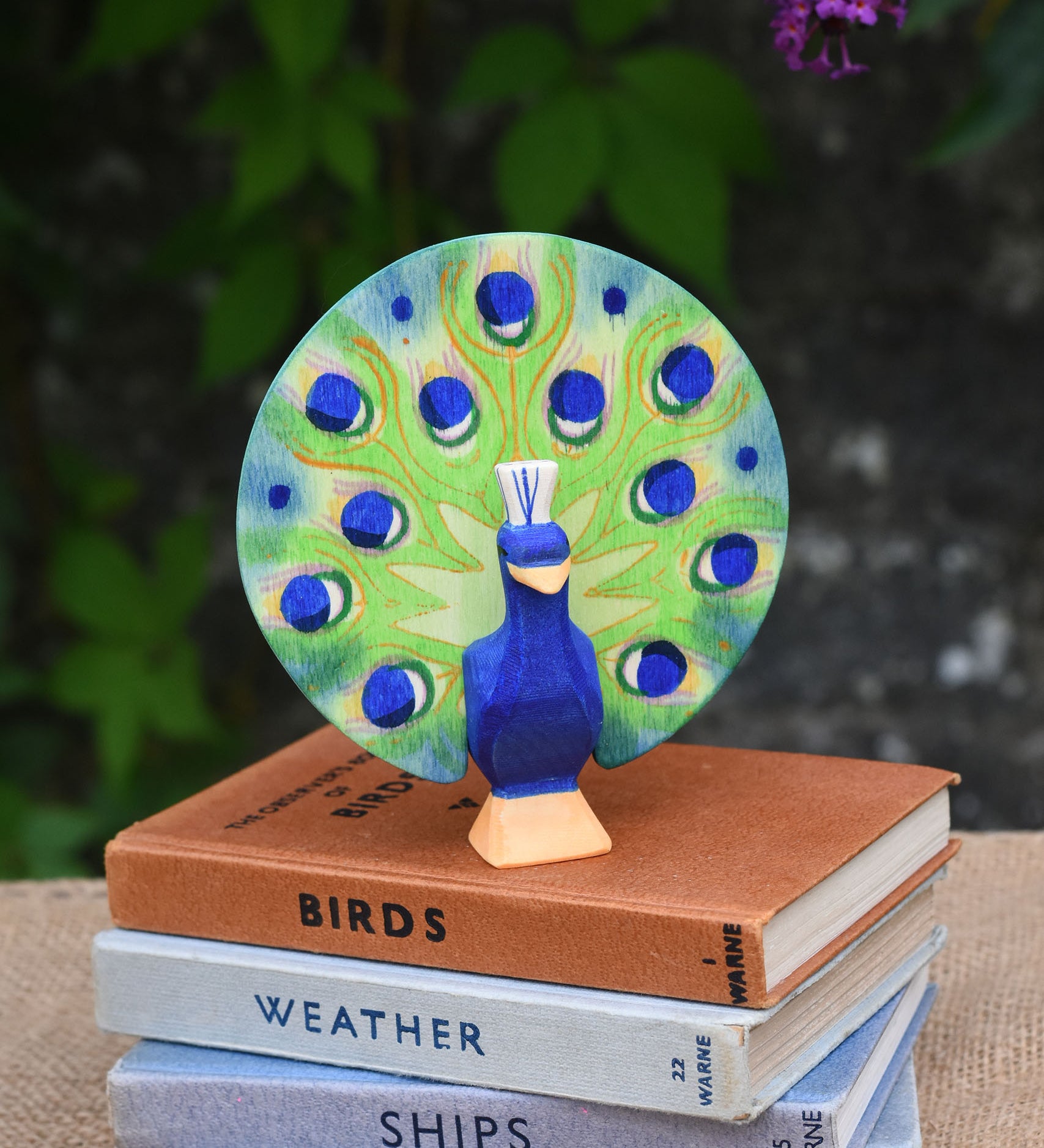 A Ostheimer peacock wooden toy figure with open feathers placed on a pile of books.