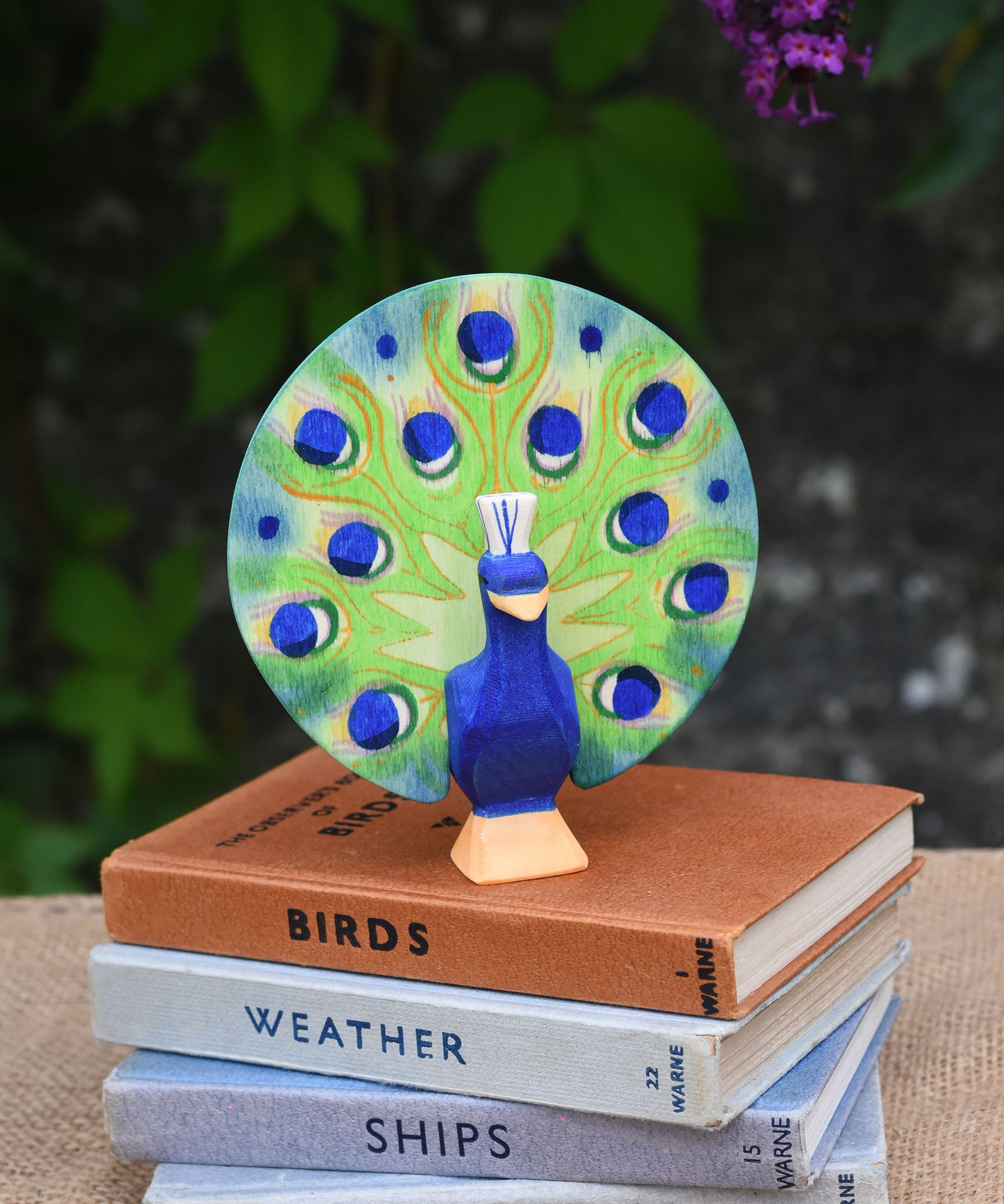 A Ostheimer peacock wooden toy figure with open feathers placed on a pile of books.