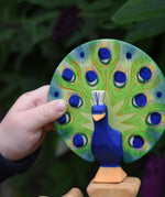 A close up of a child's hand holding the Ostheimer peacock wooden toy figure with open feathers.