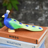 An Ostheimer peacock wooden toy figure with it's feathersdown  placed on a pile of books.