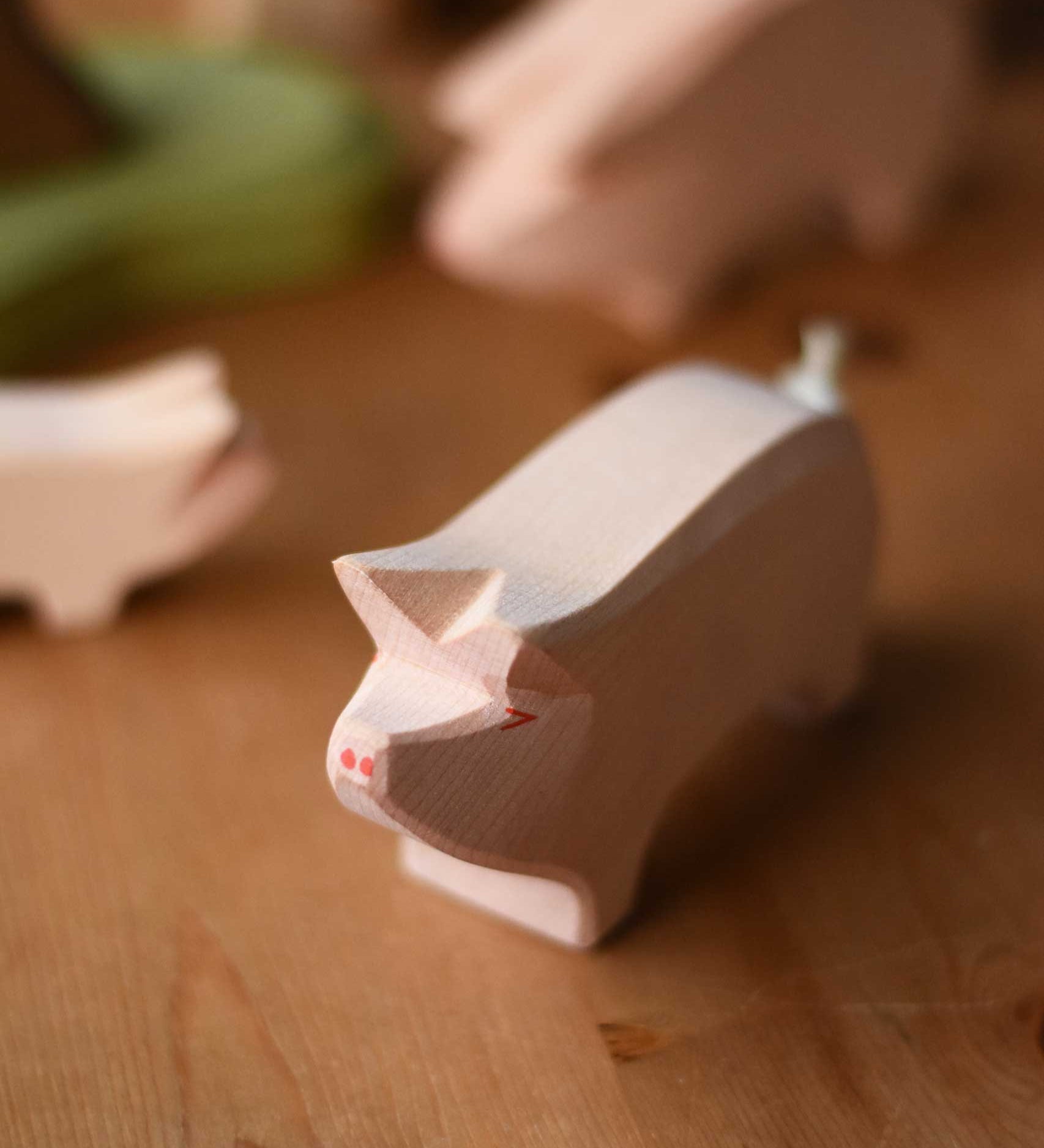 Ostheimer Pig with it's Head High placed on a wooden surface. This pink pig has a little curled rope tail.  These wooden figures are part of a wide range of expertly hand crafted wooden toys here at Babipur. 