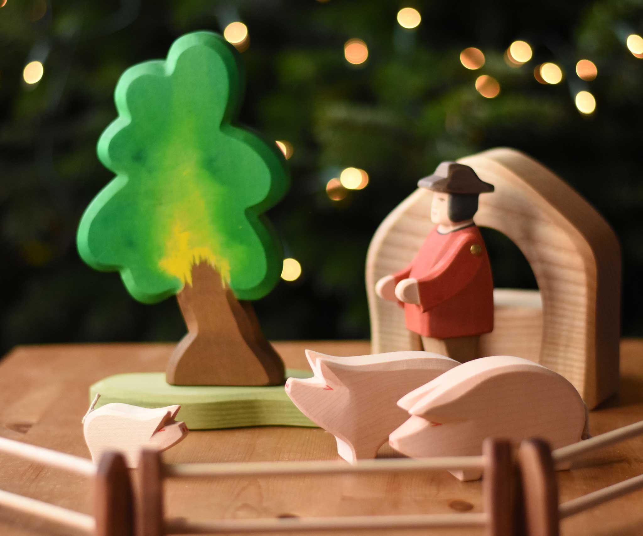 Ostheimer wooden toy pink pig and piglet figures set up in a small world play scene with the Ostheimer oak tree, farmer figure, fences and pieces from the 4 piece house set. These wooden figures are part of a wide range of expertly hand crafted wooden toys here at Babipur. 