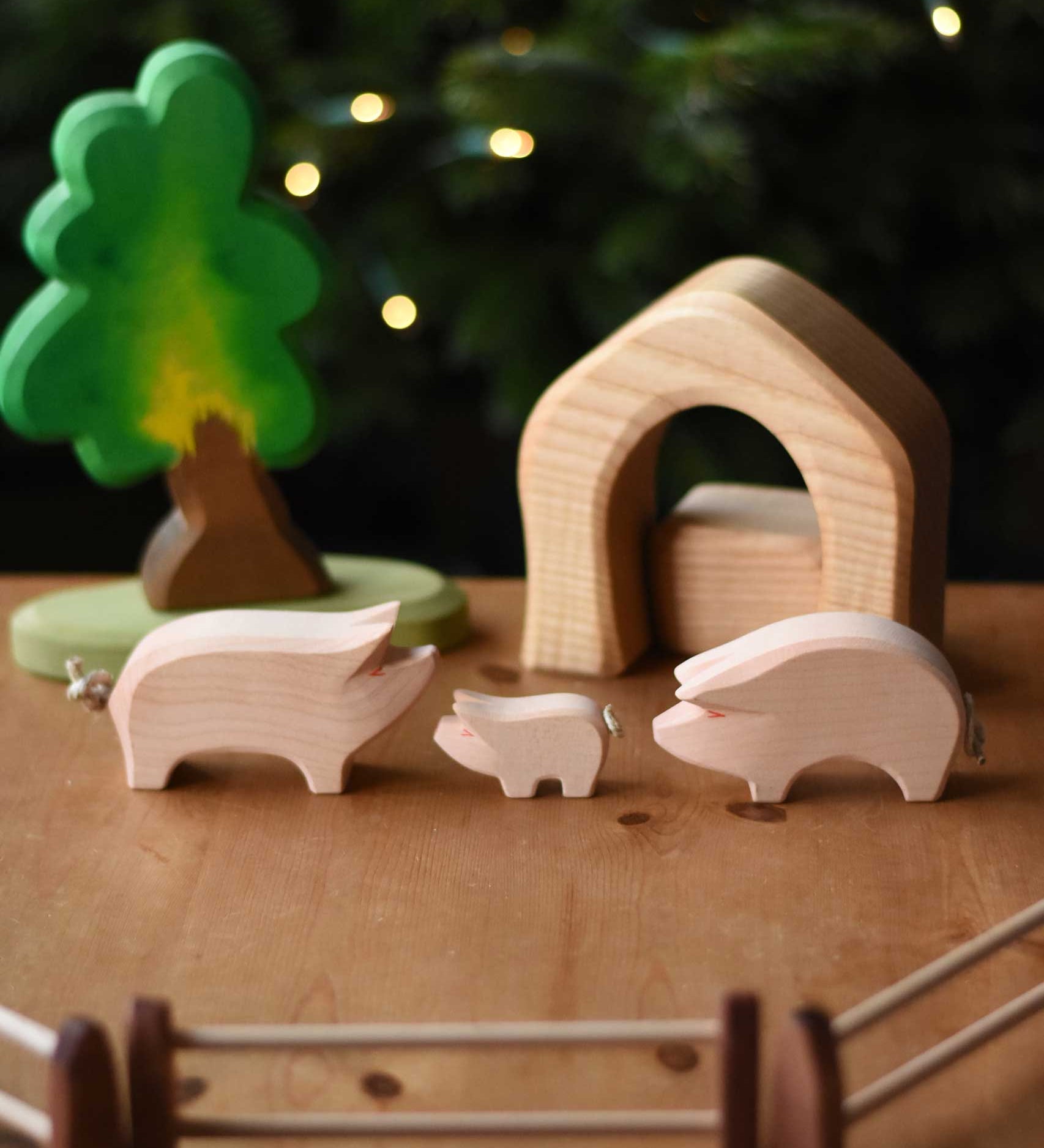 Ostheimer wooden toy pink pig and piglet figures set up in a small world play scene with the Ostheimer oak tree, fences and pieces from the 4 piece house set. These wooden figures are part of a wide range of expertly hand crafted wooden toys here at Babipur. 